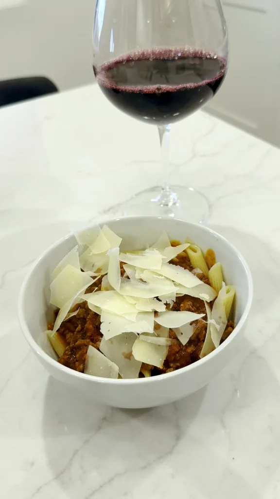 A bowl of pasta with Michael's sauce, shaved parmesan and a glass of red wine